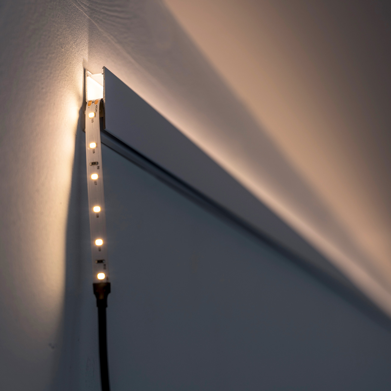 Warm white LED strip attached to a wall beside a doorway, with a black power cord hanging down.