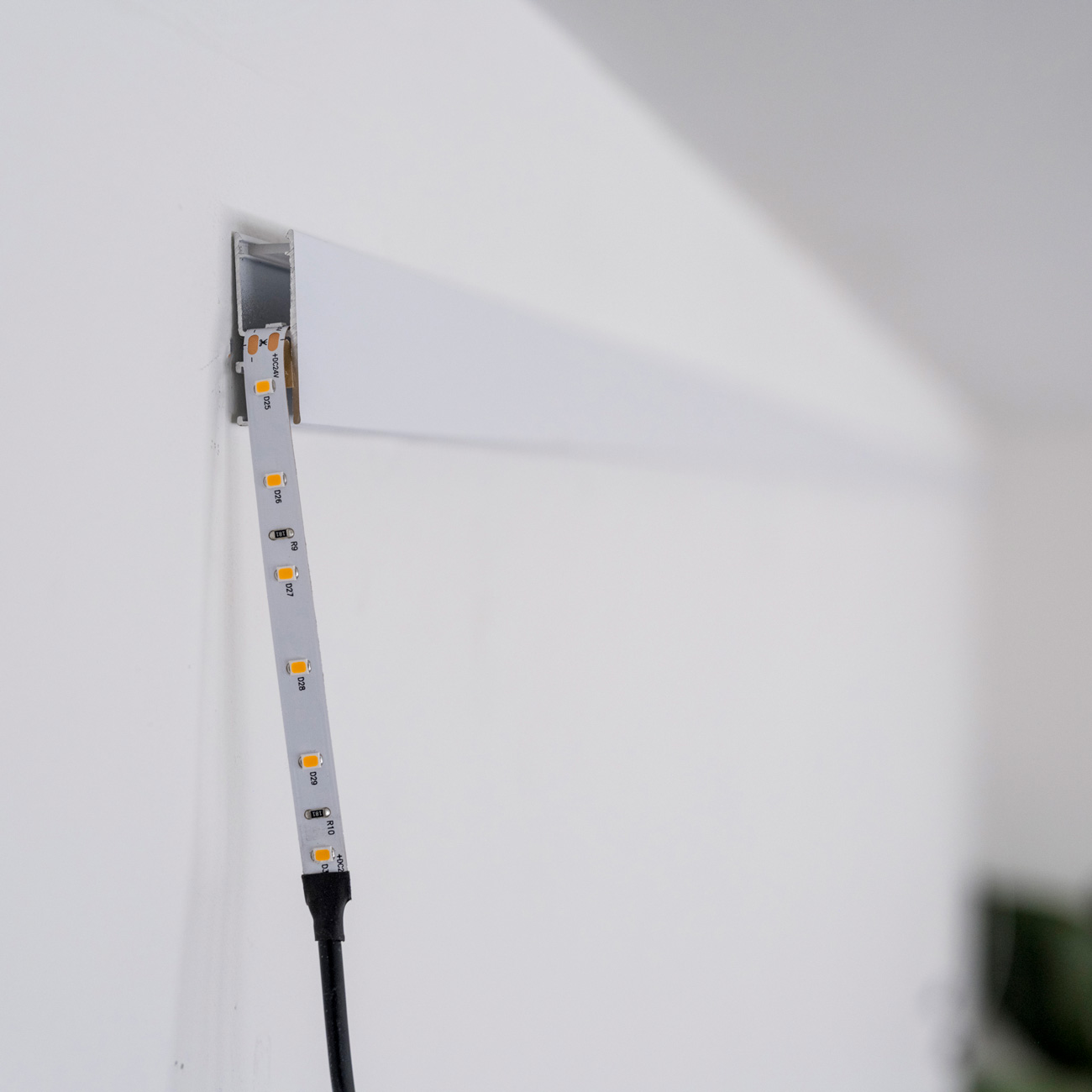 LED strip light being inserted into a wall channel, with yellow diode chips and a black power cable visible