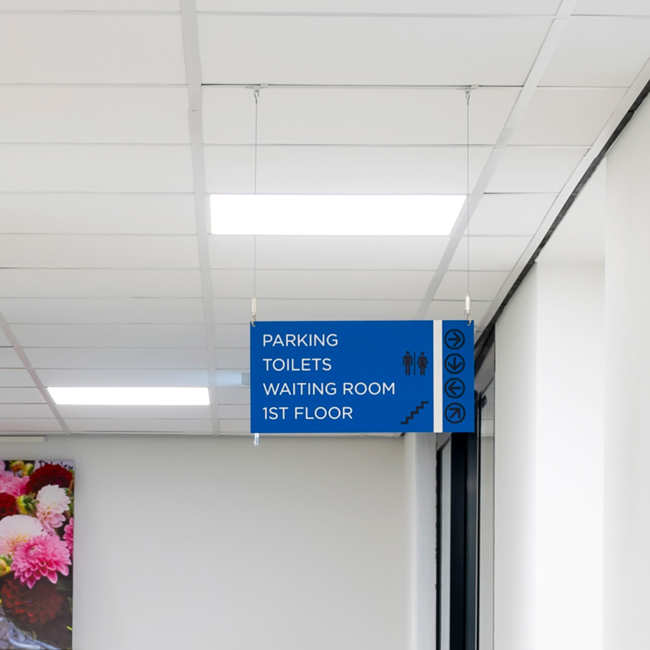 Blue indoor sign listing: Parking, Toilets, Waiting Room, 1st Floor with directional icons and arrows to the right.