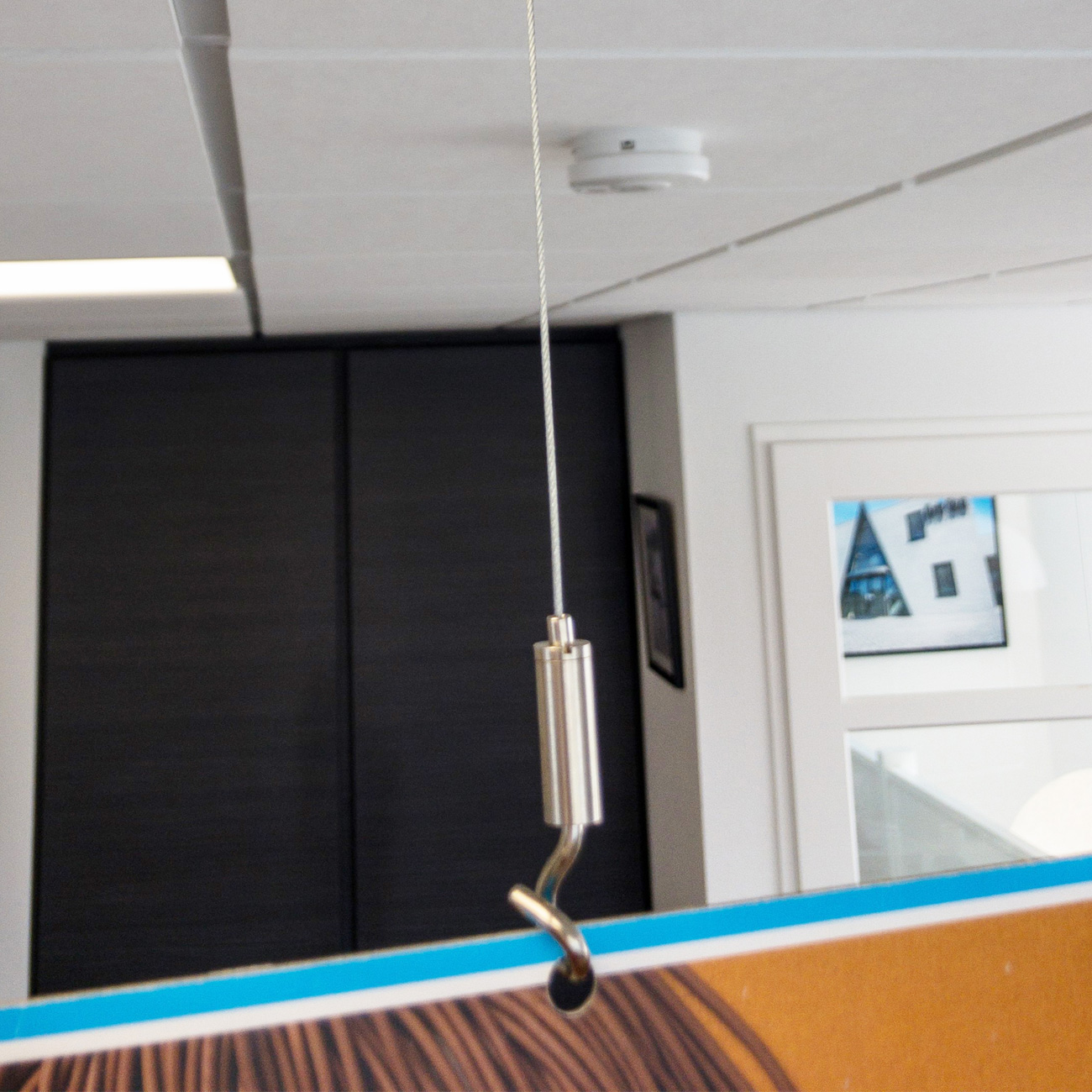 Silver pendant light hanging from a braided cord in a modern office, with dark cabinets and a white door in the background.