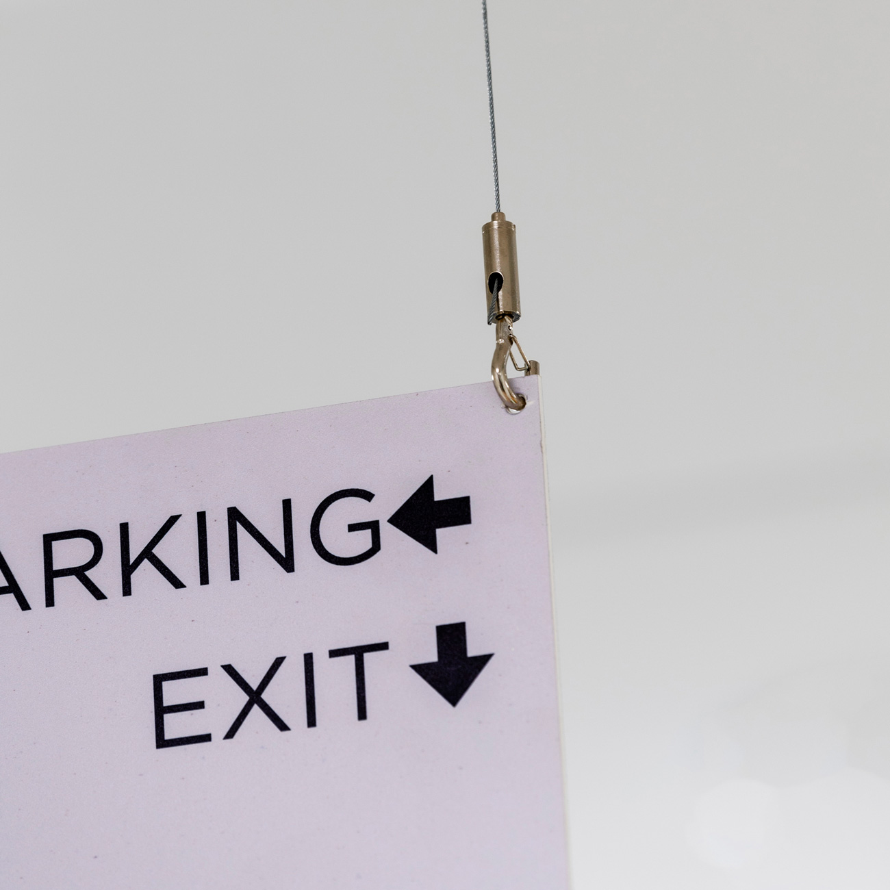 Hanging sign reading 'PARKING' with a left-pointing arrow and 'EXIT' with a down arrow, attached by a metal hook.