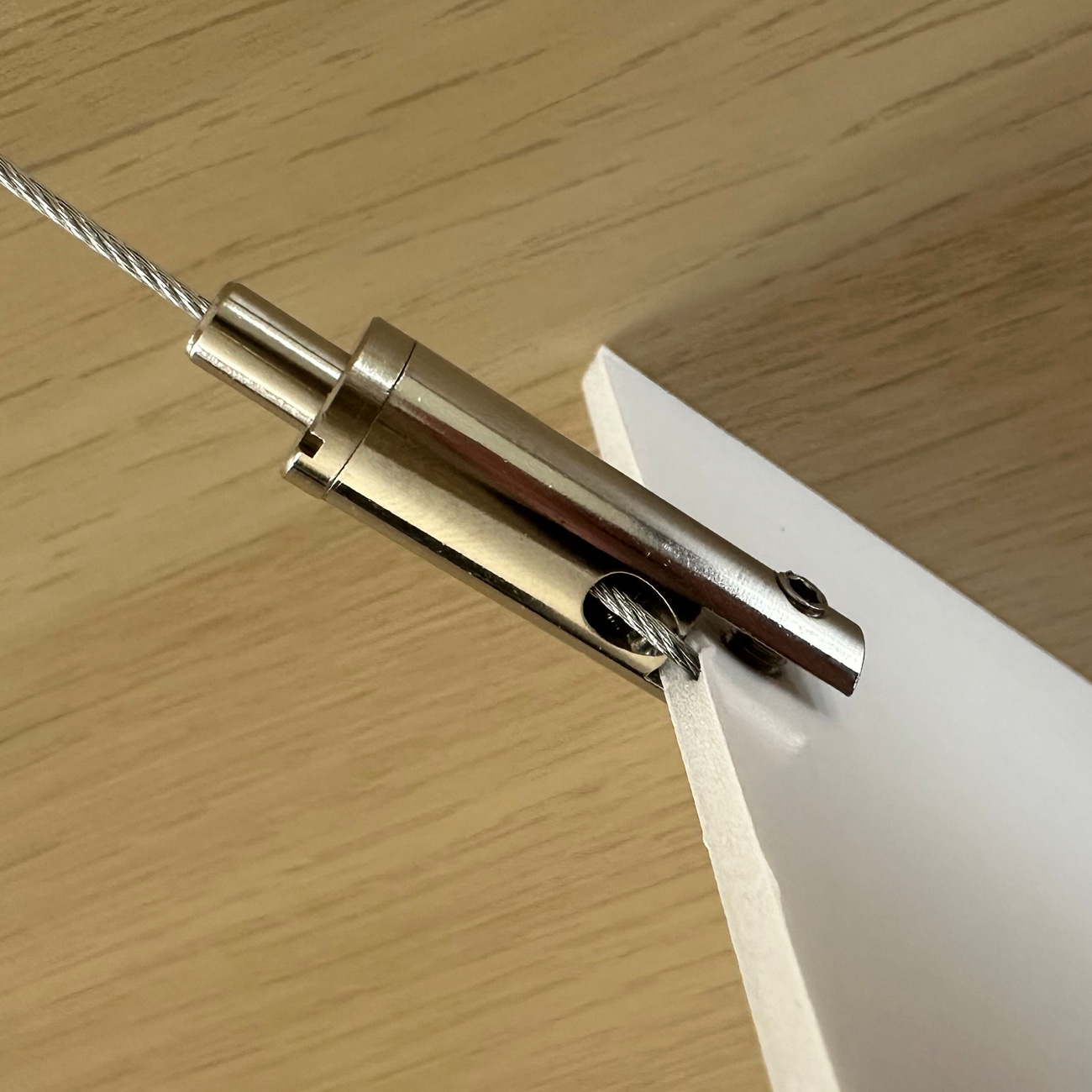 Close-up of a metal cable clamp holding a thin steel wire to a white sheet on a wooden surface.